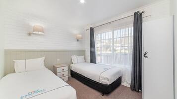 A hotel room with two beds, a white brick wall, a window with curtains, and a door.