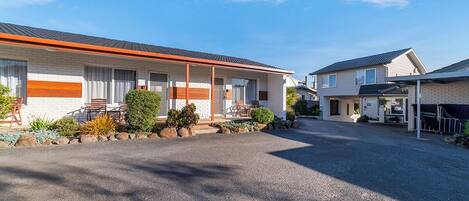 A motel with a gravel driveway, a covered parking area, and a small garden with plants and rocks.