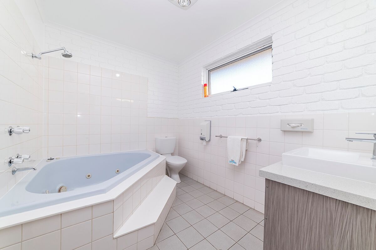 Un baño moderno con una bañera independiente, un inodoro, un lavabo y un ventanal sobre el lavabo.