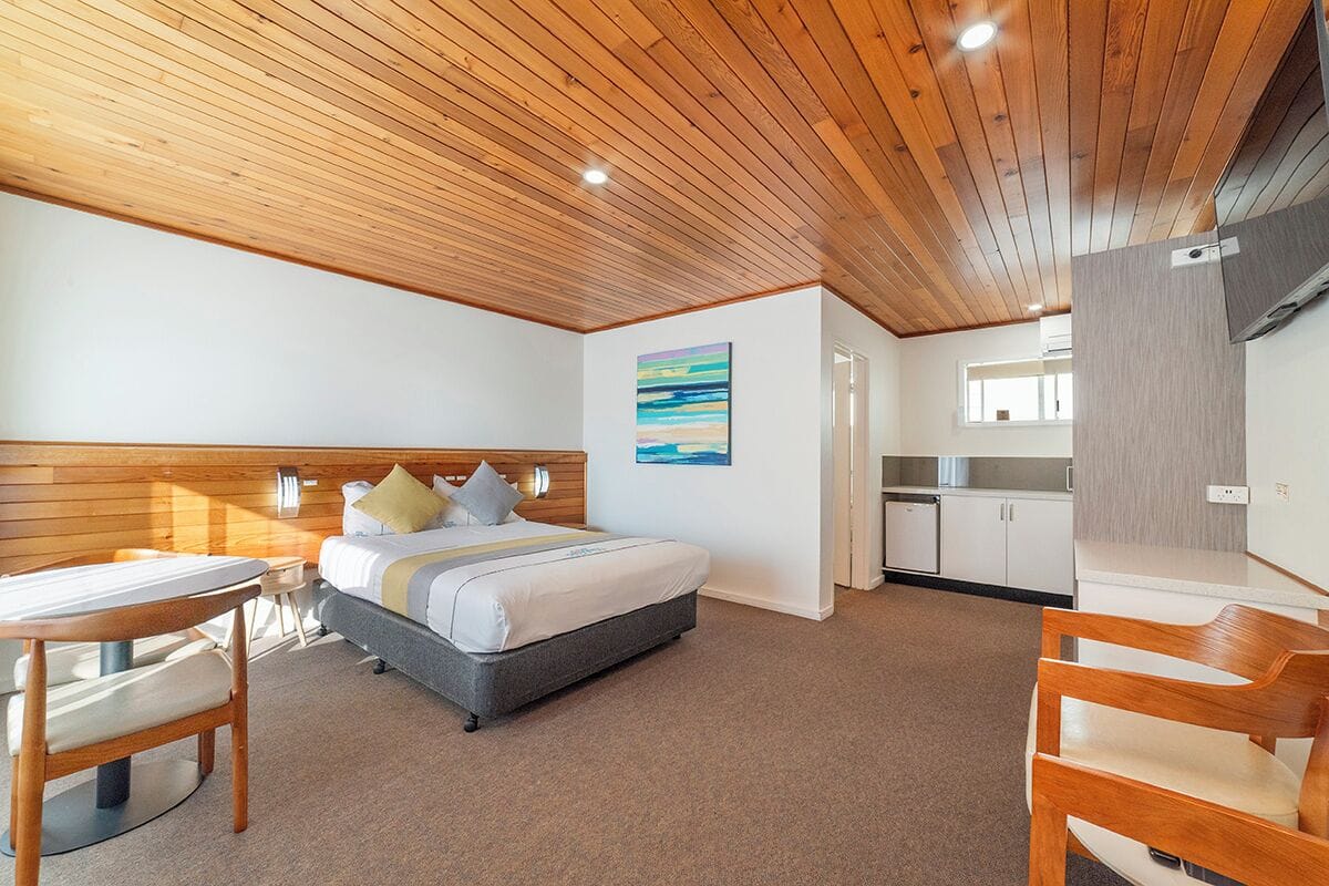 Ein Schlafzimmer mit Holzbalkendecke, einem Bett, einem Schreibtisch und einem Sessel.