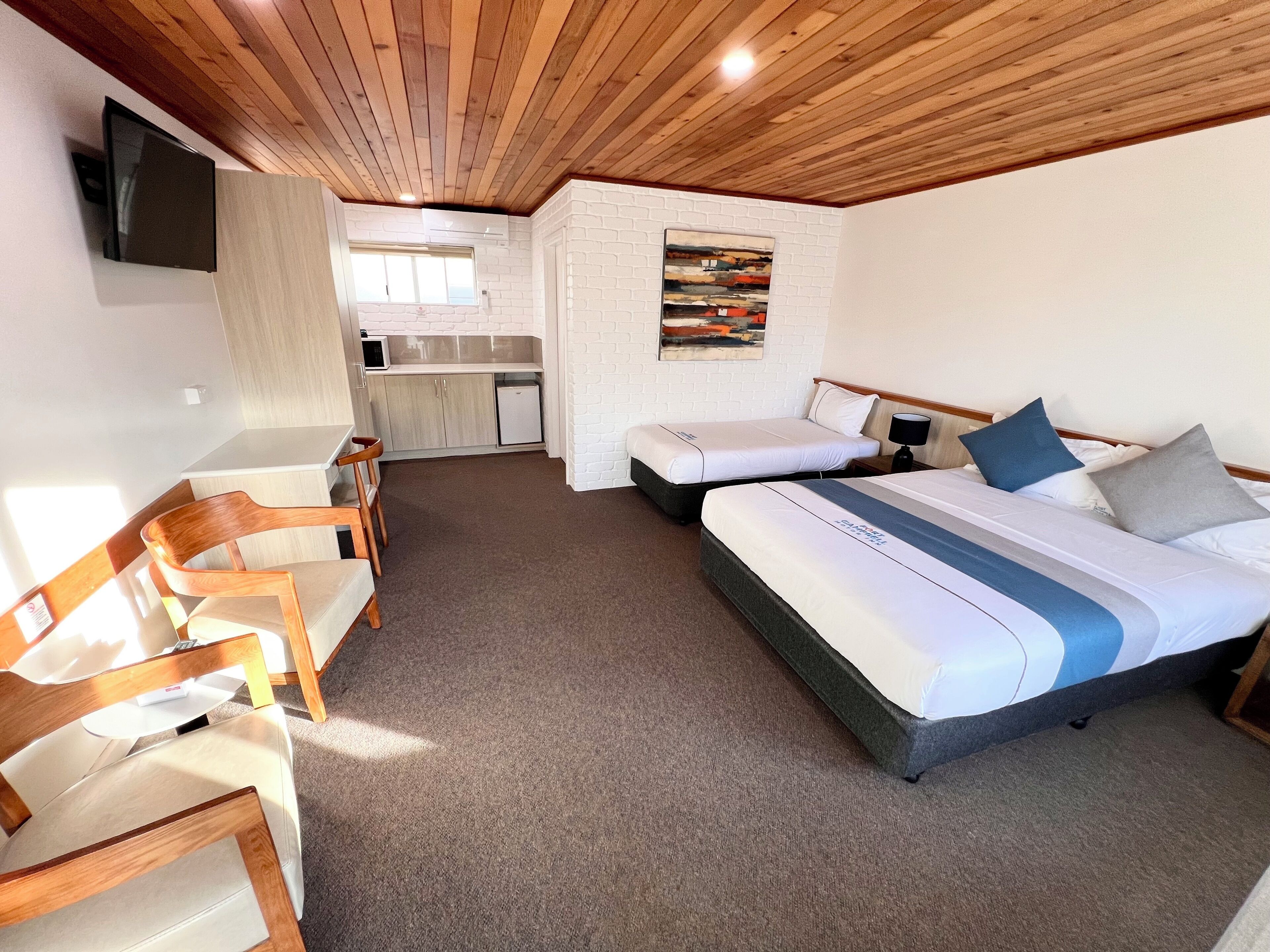 Habitación de hotel con techo de madera, kitchenette, zona de comedor con sillas y cama con almohadas.