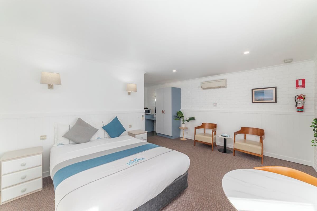 Ein Hotelzimmer mit einem Bett, Nachttischen, einem Schreibtisch, einem Sessel und einem kleinen Tisch.