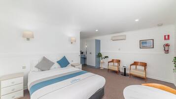 Una habitación de hotel con cama, mesitas de noche, escritorio, silla y una pequeña mesa.