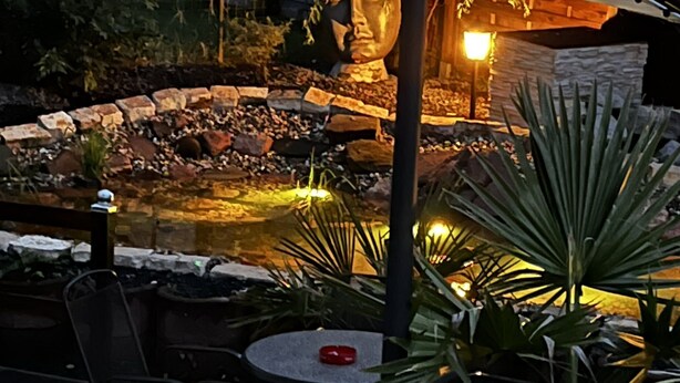 Uma área de estar ao ar livre com parede de pedra, um pequeno espelho d'água e plantas em vasos.