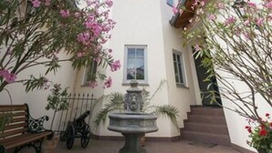 Um pátio com uma fonte, um banco e um edifício com telhado de azulejos e várias janelas.