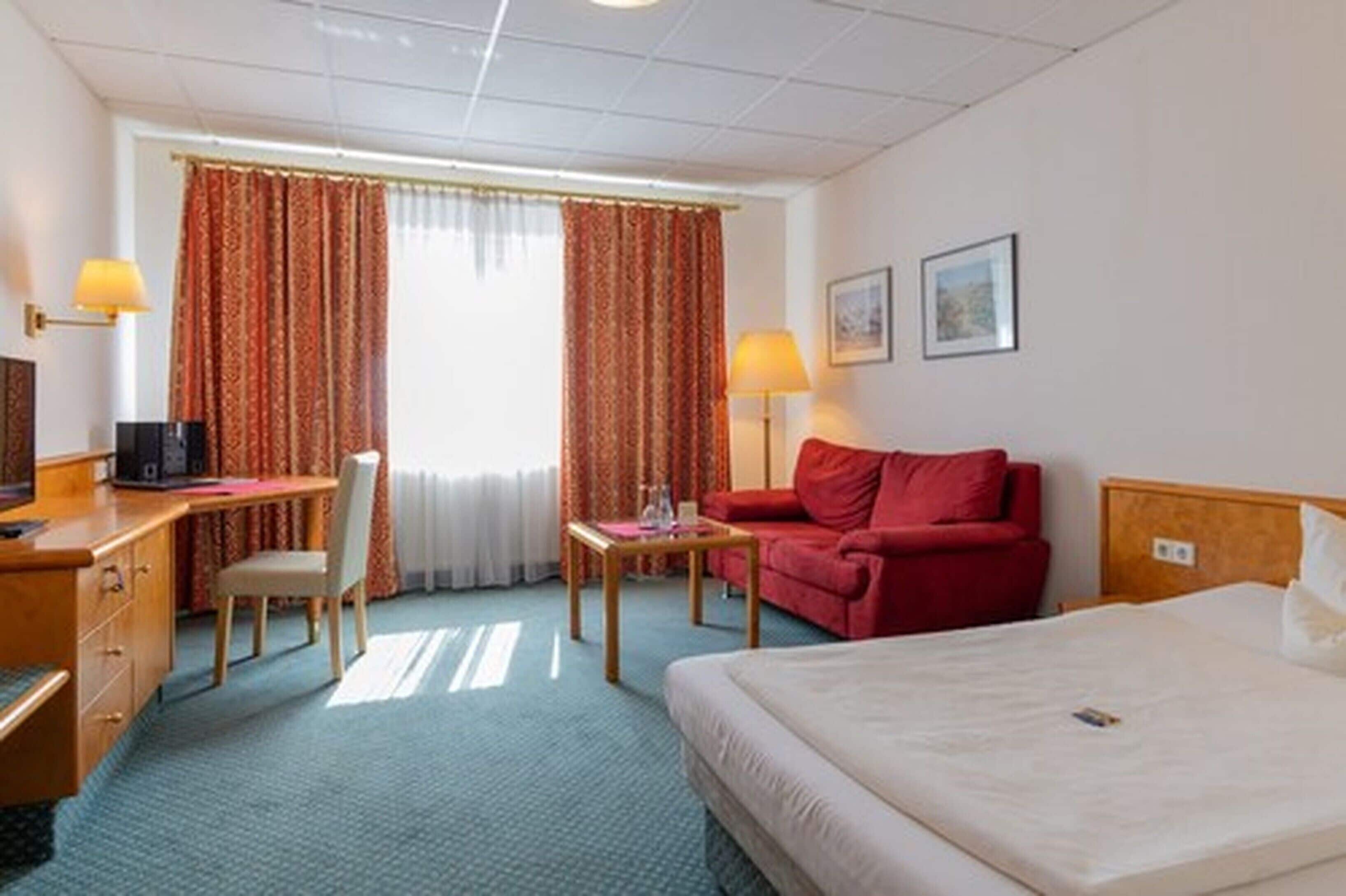 Ein Hotelzimmer mit einem Bett, einem Schreibtisch mit Stuhl, einem roten Sofa und zwei Lampen.