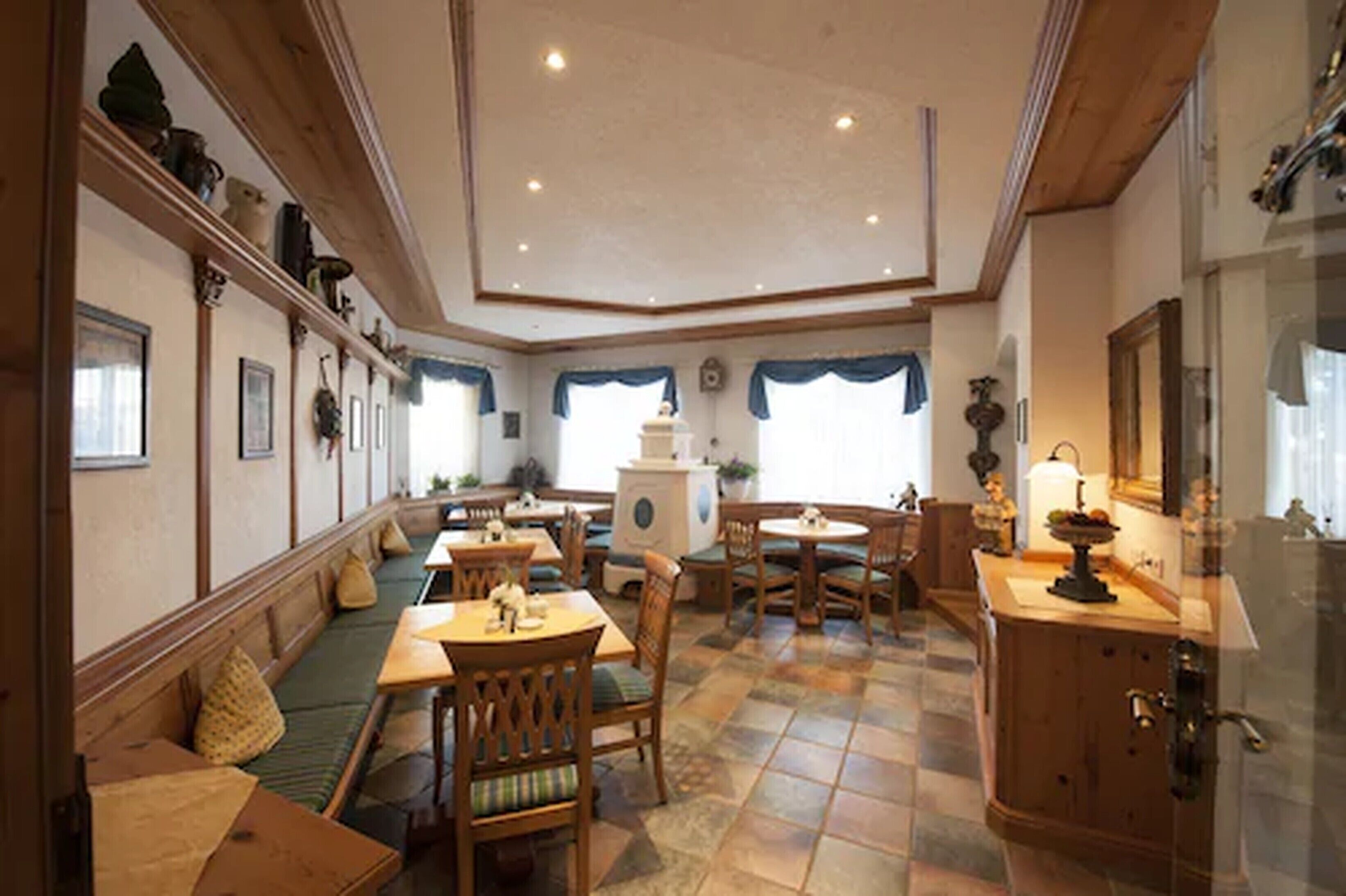 A dining area with wooden tables and benches, a kitchen counter, and a large window with blue curtains.