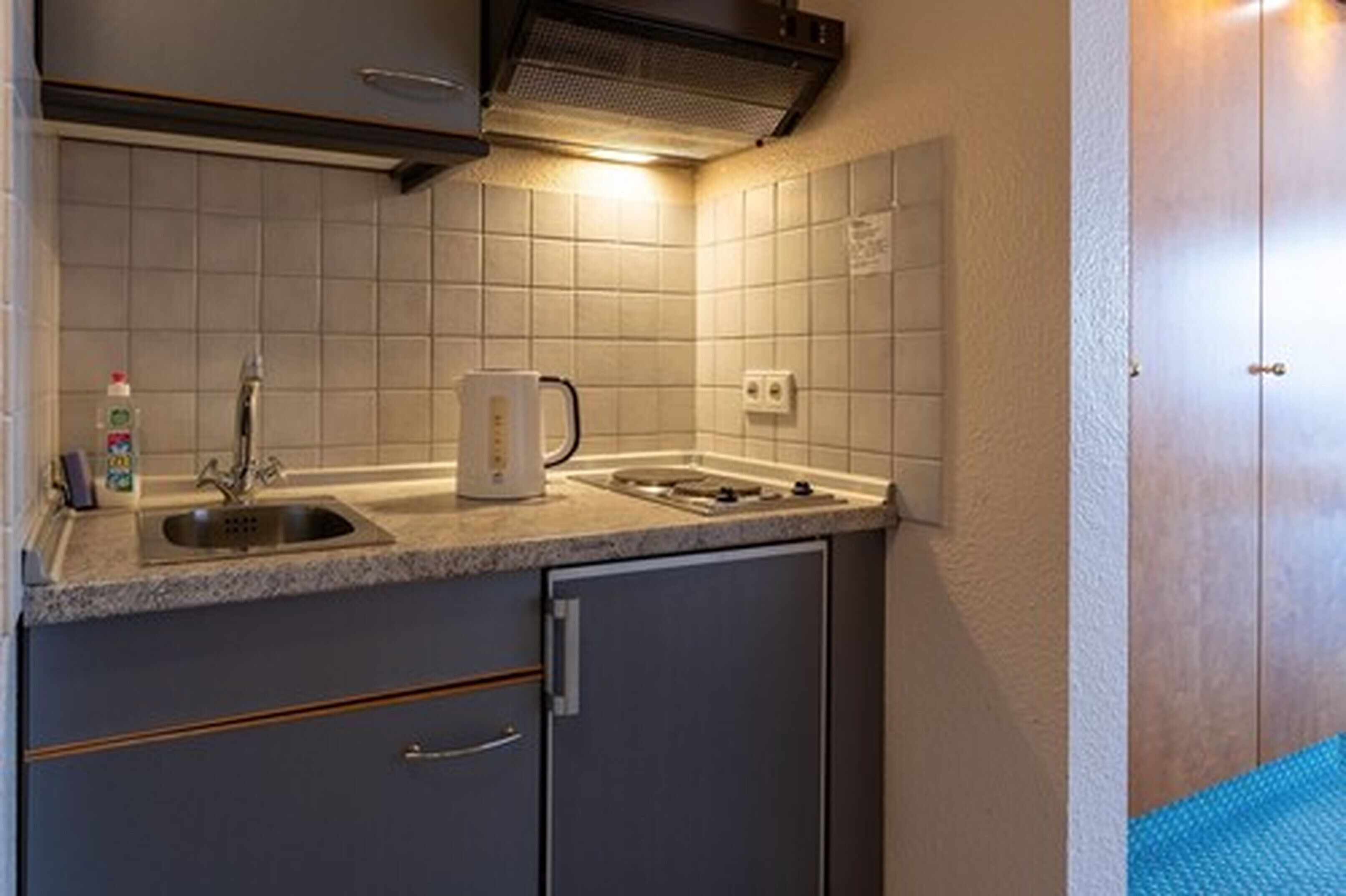 Una cocina compacta con lavamanos, estufa y hervidor.