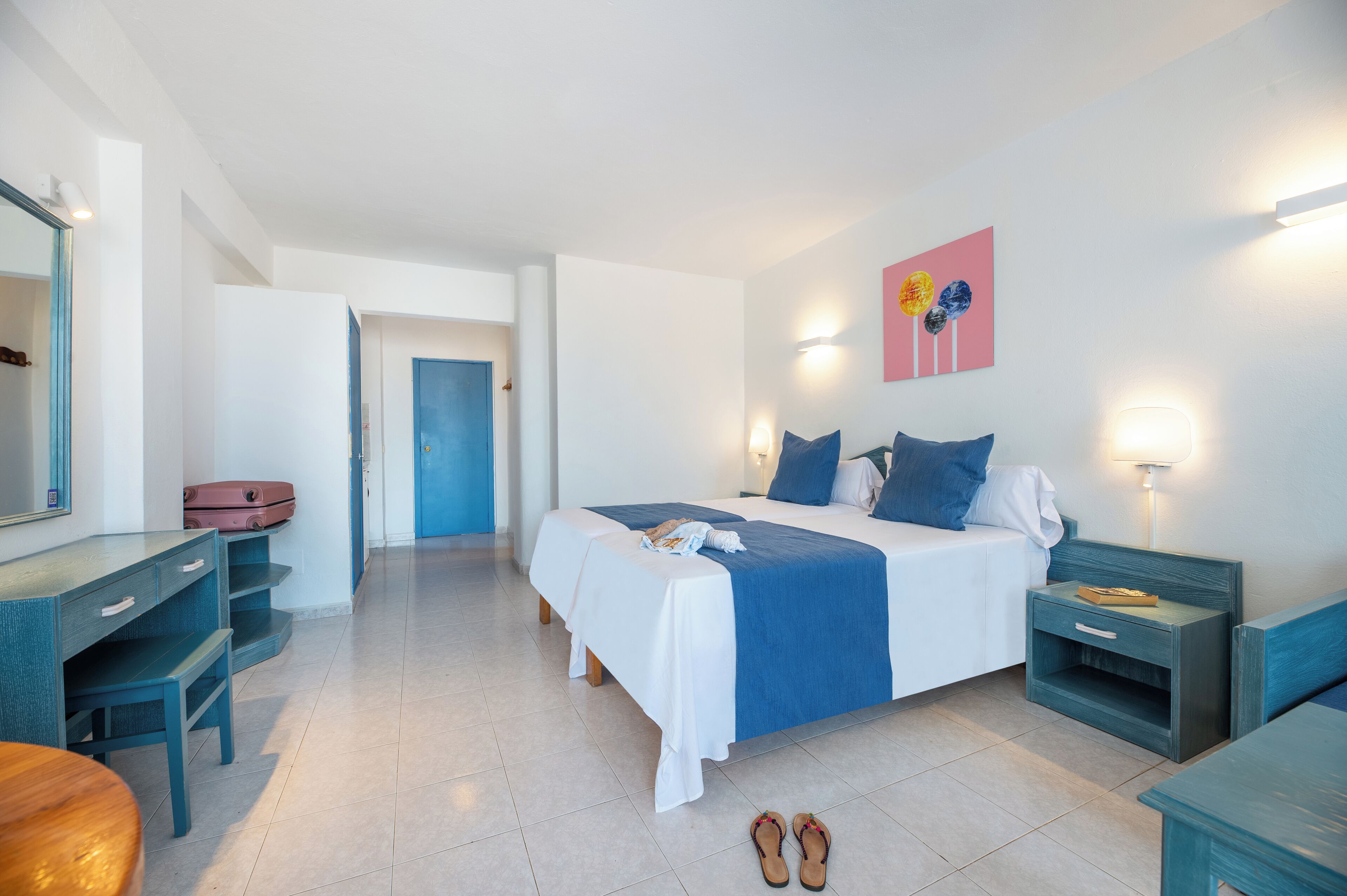 Ein Schlafzimmer mit Bett, Nachttischen, Schreibtisch, Spiegel und Tür.