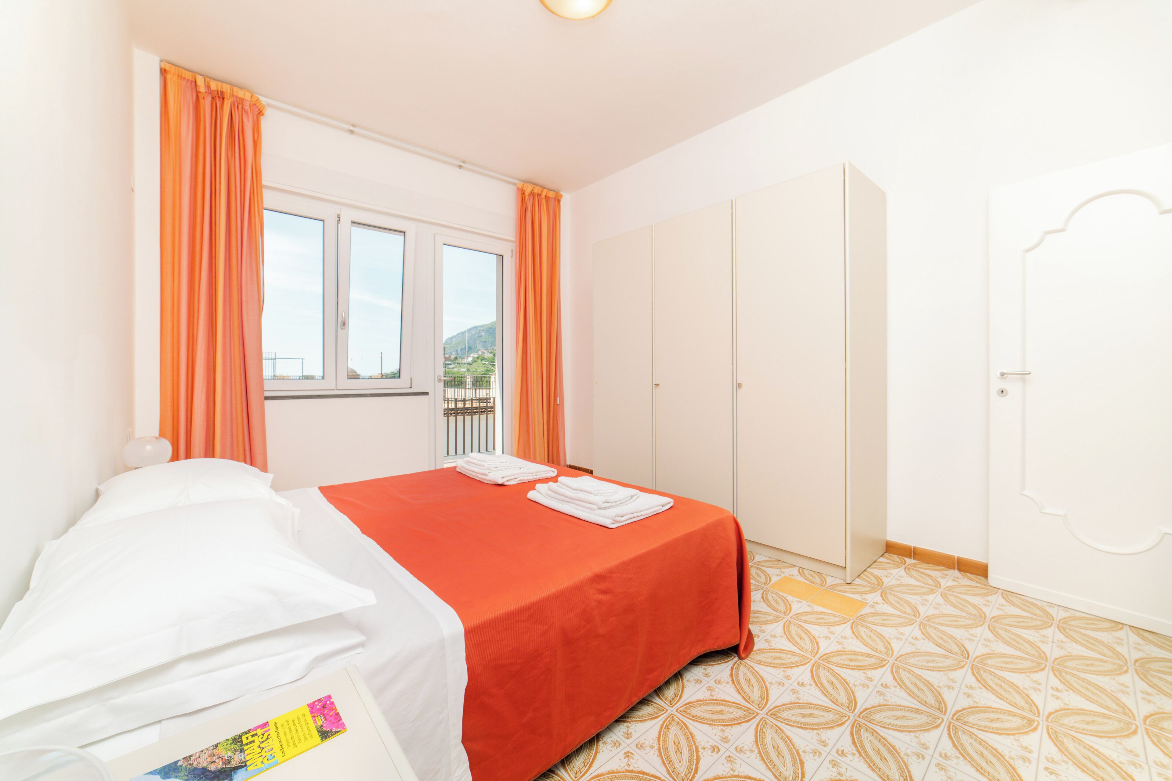 Una habitación con cama, ventana con cortinas, armario y suelo estampado.