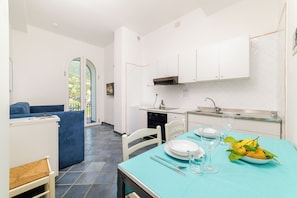 A modern kitchen with white cabinets, a dining table with a blue tablecloth, and a view of the outdoors through a glass door.