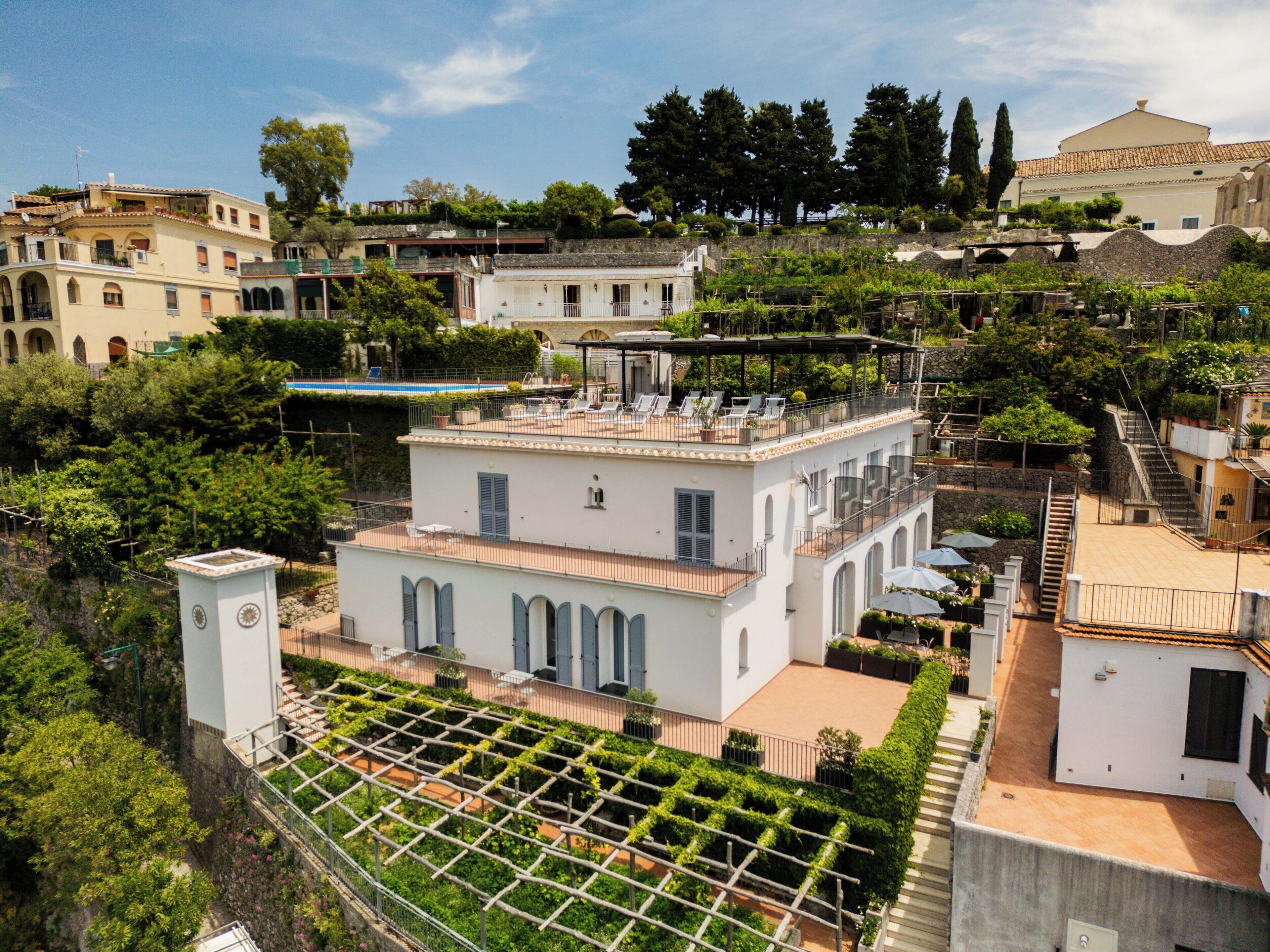 A multi-story building with a rooftop terrace, a garden area with a trellis, and a staircase leading to an upper level.