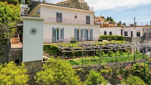 A two-story building with a balcony, a garden with a pergola, and a stone wall. - Residence Le Villette (Ravello)