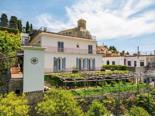 A two-story building with a balcony, a garden with a pergola, and a stone wall. - Residence Le Villette (Ravello)