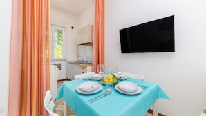 A dining area with a table set for two, a flat-screen TV mounted on the wall, and a window with curtains. - Residence Le Villette (Ravello)