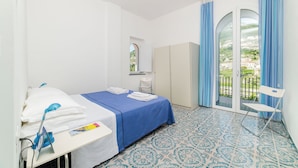 A hotel room with a bed, a desk, a chair, a wardrobe, and a view of a balcony with a railing. - Residence Le Villette (Ravello)