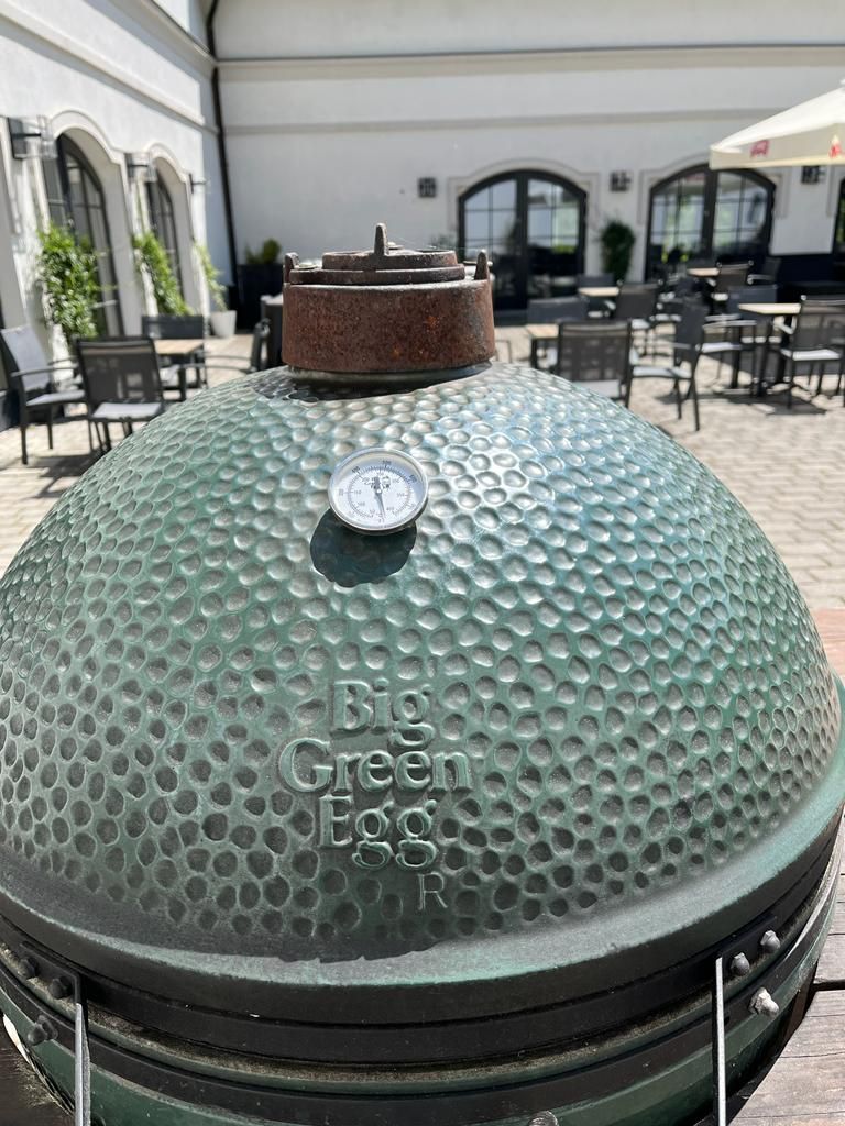 A large, textured outdoor grill with a thermometer on top, set on a patio with outdoor seating.
