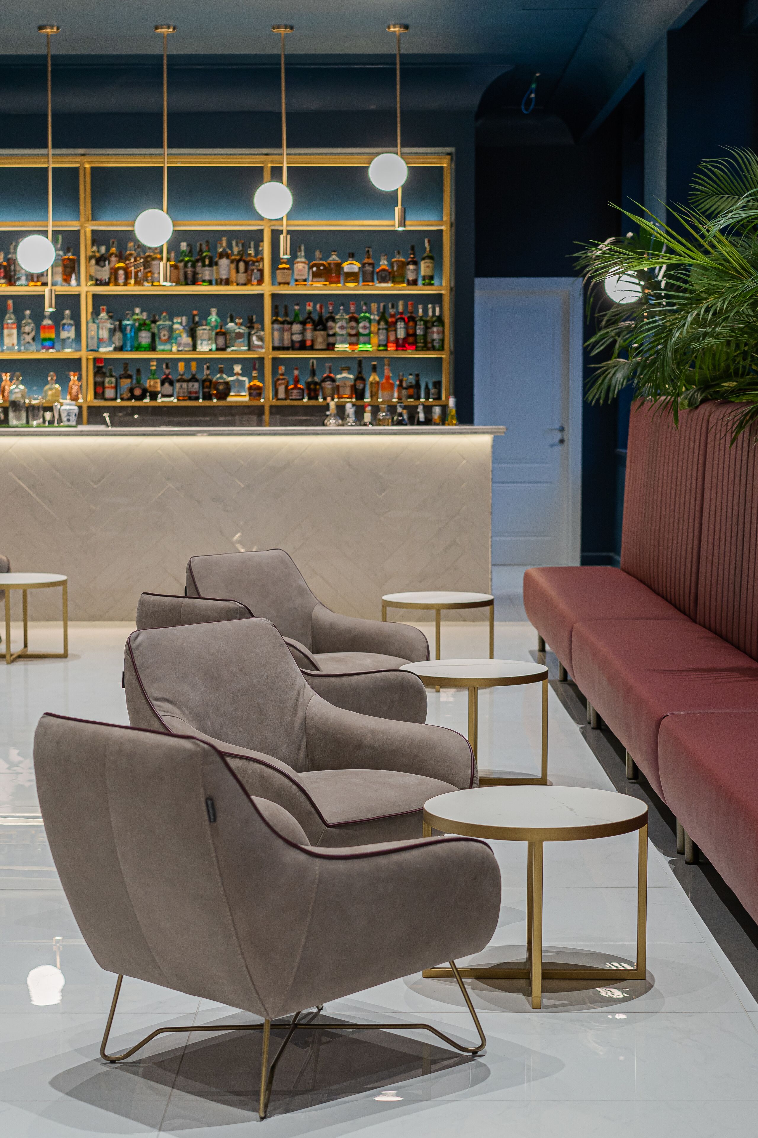 A modern bar area with a bar counter, multiple shelves of bottles, and seating with round tables.