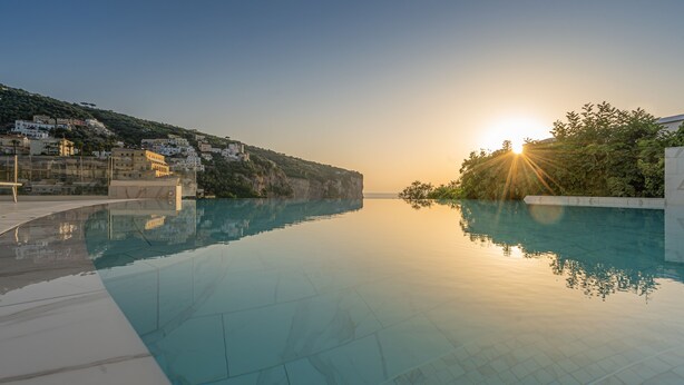 A clear swimming pool with a view of a hillside and buildings in the background.