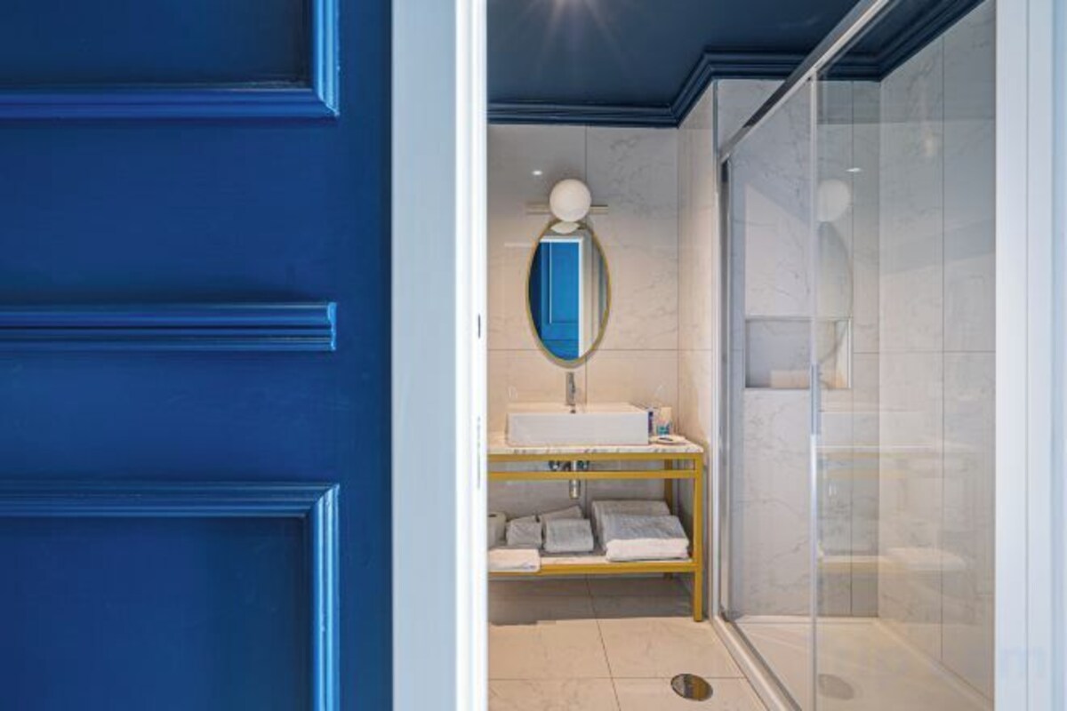A bathroom with a blue door, a white sink, a mirror, and a glass shower enclosure.