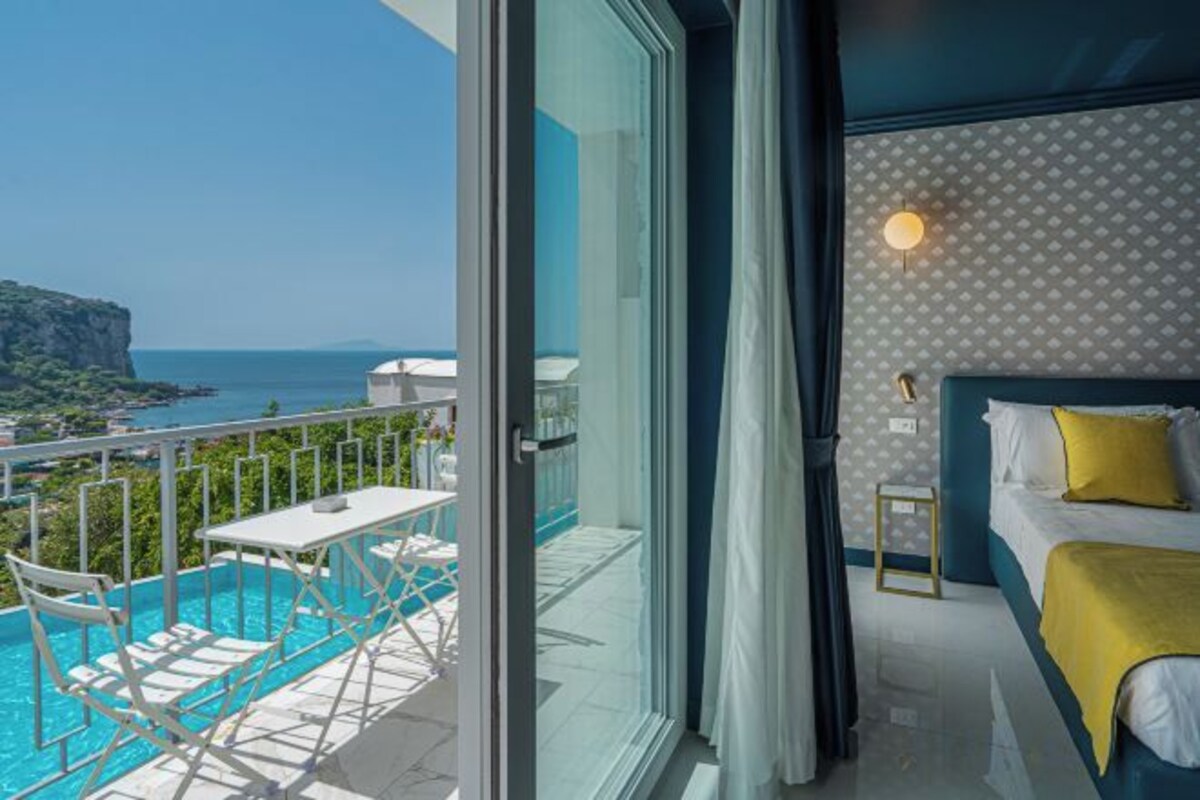 A balcony with a pool, a bed with a yellow throw, and a view of the sea.
