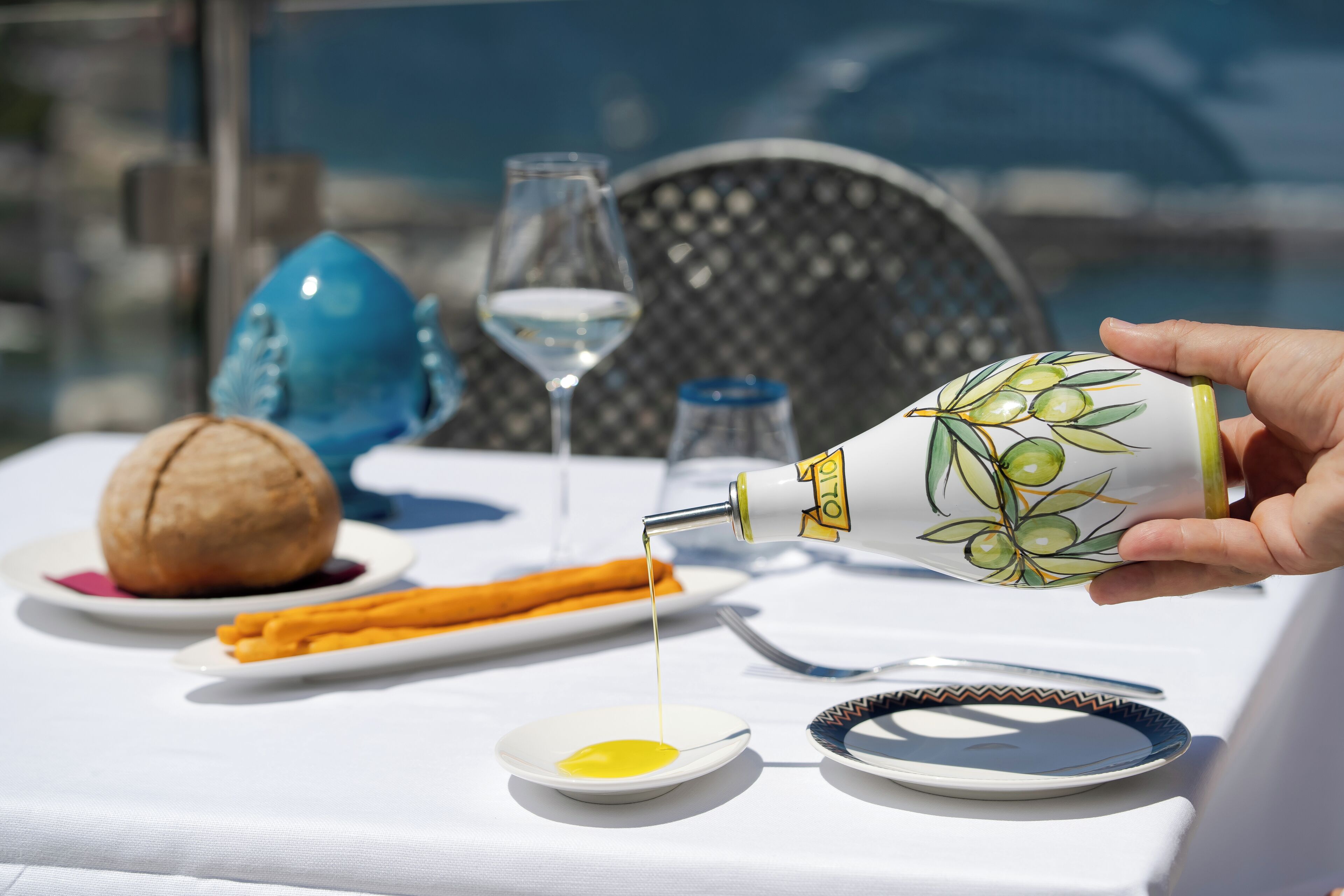 Una mesa con una botella de aceite de oliva, una copa de vino blanco, un coco y un plato con rodajas de naranja.