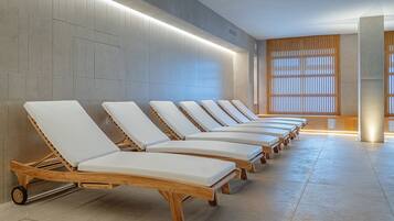 A row of wooden lounge chairs with white cushions in a modern spa setting.