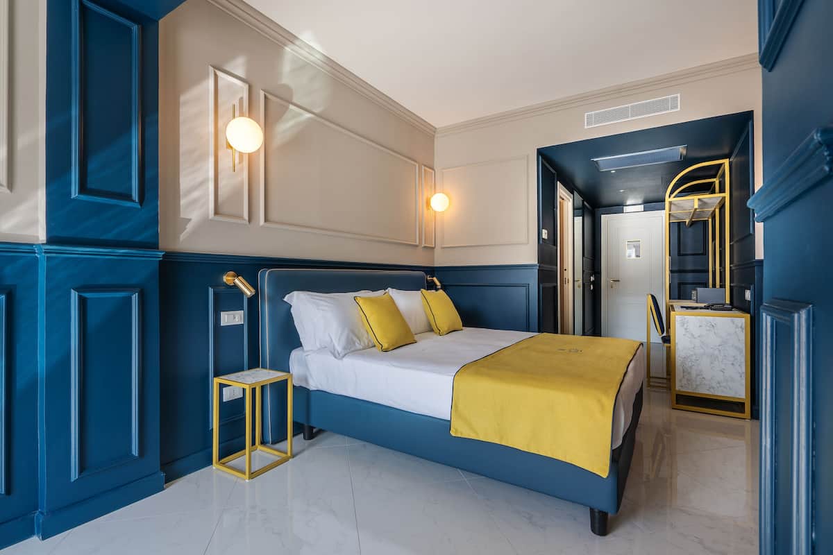 Un dormitorio moderno con una paleta de colores azul y blanco, una cama con detalles amarillos y una mesita de noche pequeña.