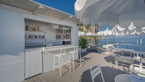 A bar area with white bar stools and a counter stocked with bottles, overlooking a body of water.
