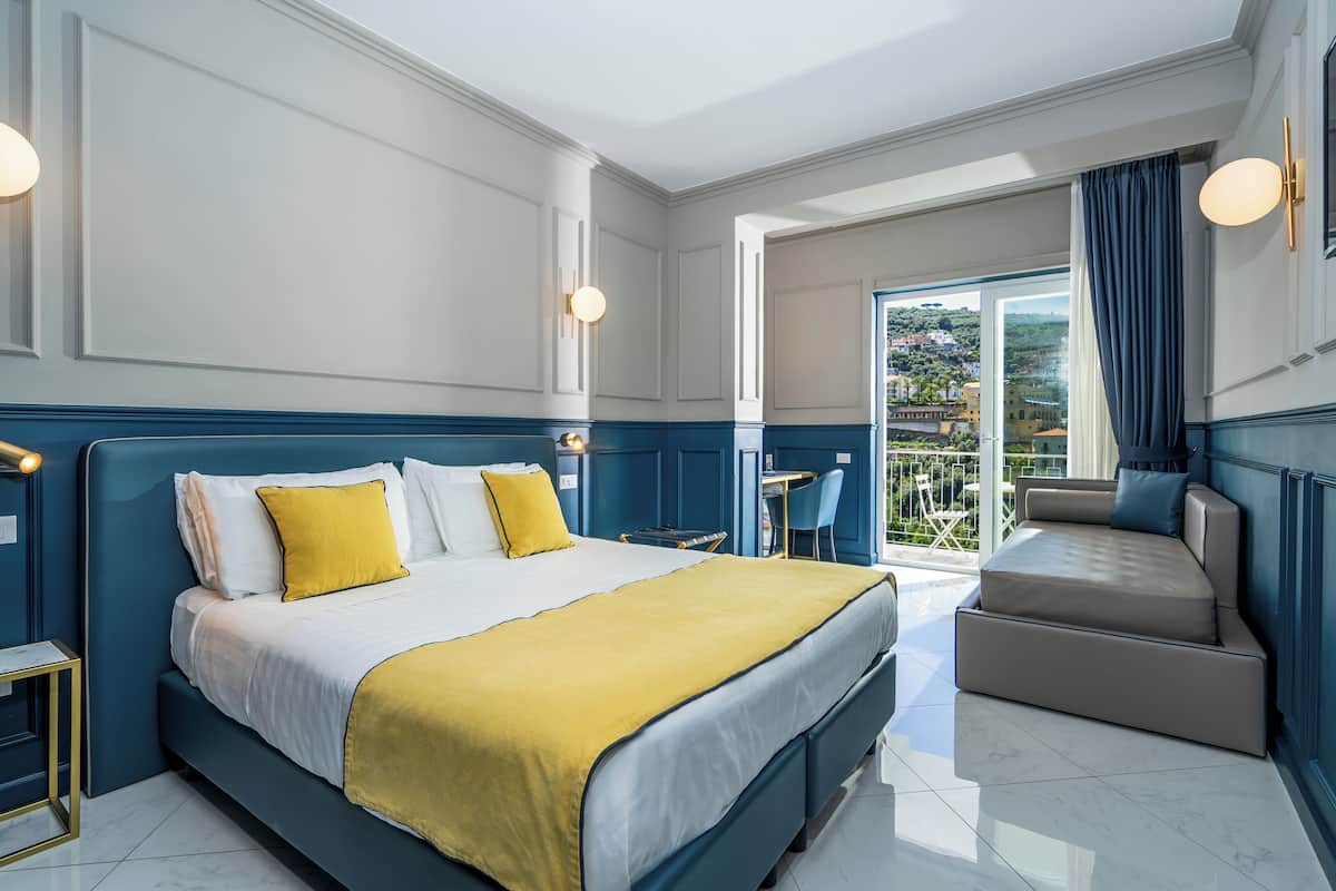 Una habitación de hotel moderna con una cama grande, un sofá, un balcón con vistas y una pequeña mesa.