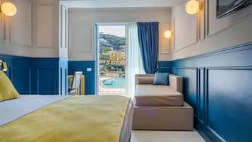A hotel room with a bed, a sofa, a view of a pool and buildings, and a TV on the wall.