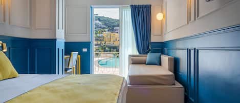 Habitación de hotel con cama, sofá, vistas a una piscina y edificios, y un televisor en la pared.