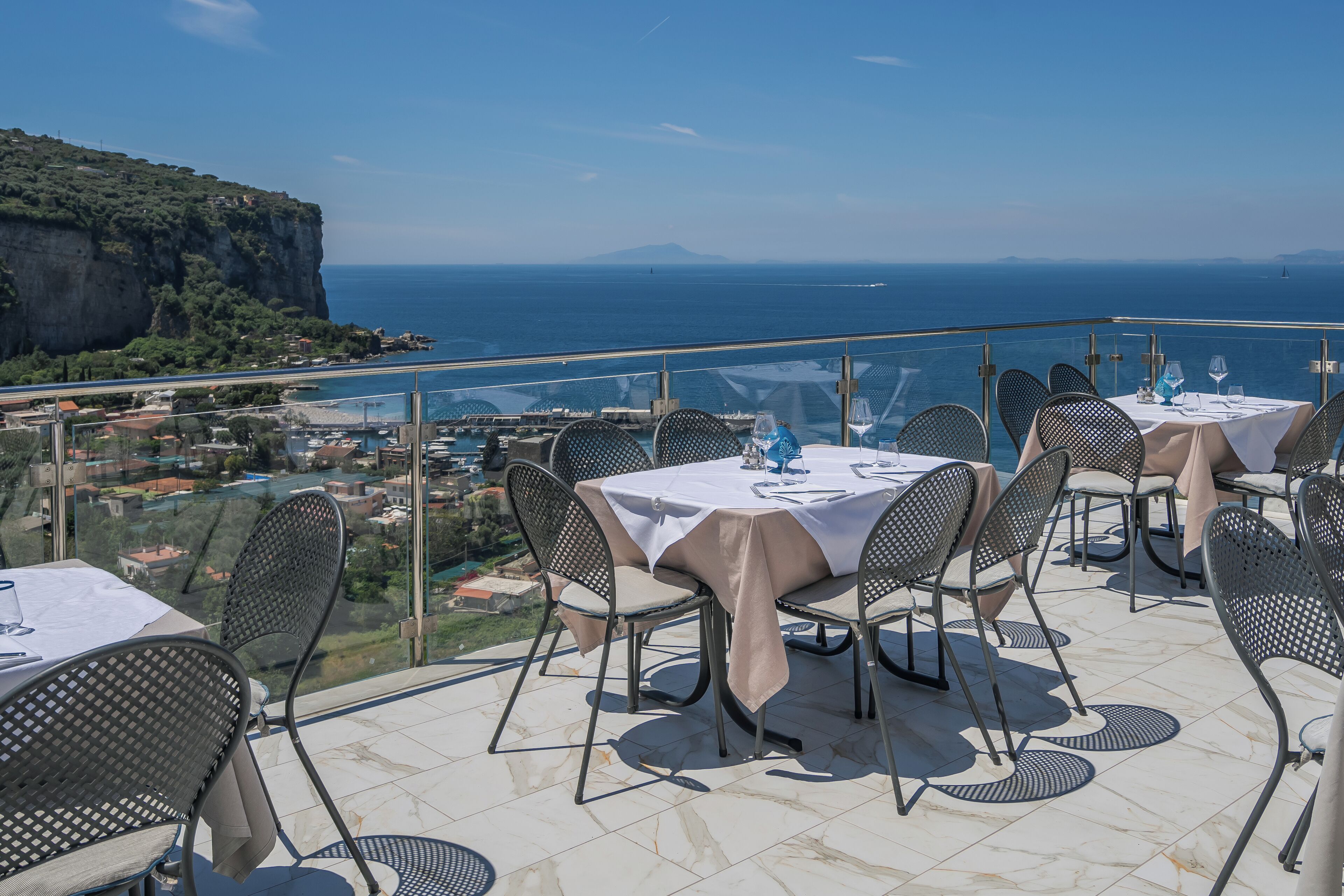 Un espace de restauration en plein air, avec des tables et des chaises, offrant une vue sur la côte, avec ses falaises et la mer.