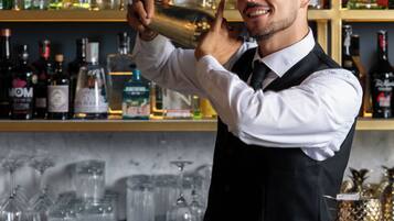 Um barman servindo uma bebida atrás do balcão, com prateleiras cheias de garrafas de bebidas.