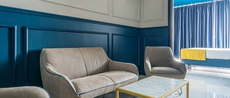 Une pièce avec un mur lambrissé bleu, un canapé beige, un fauteuil assorti et une petite table basse avec un cadre doré.