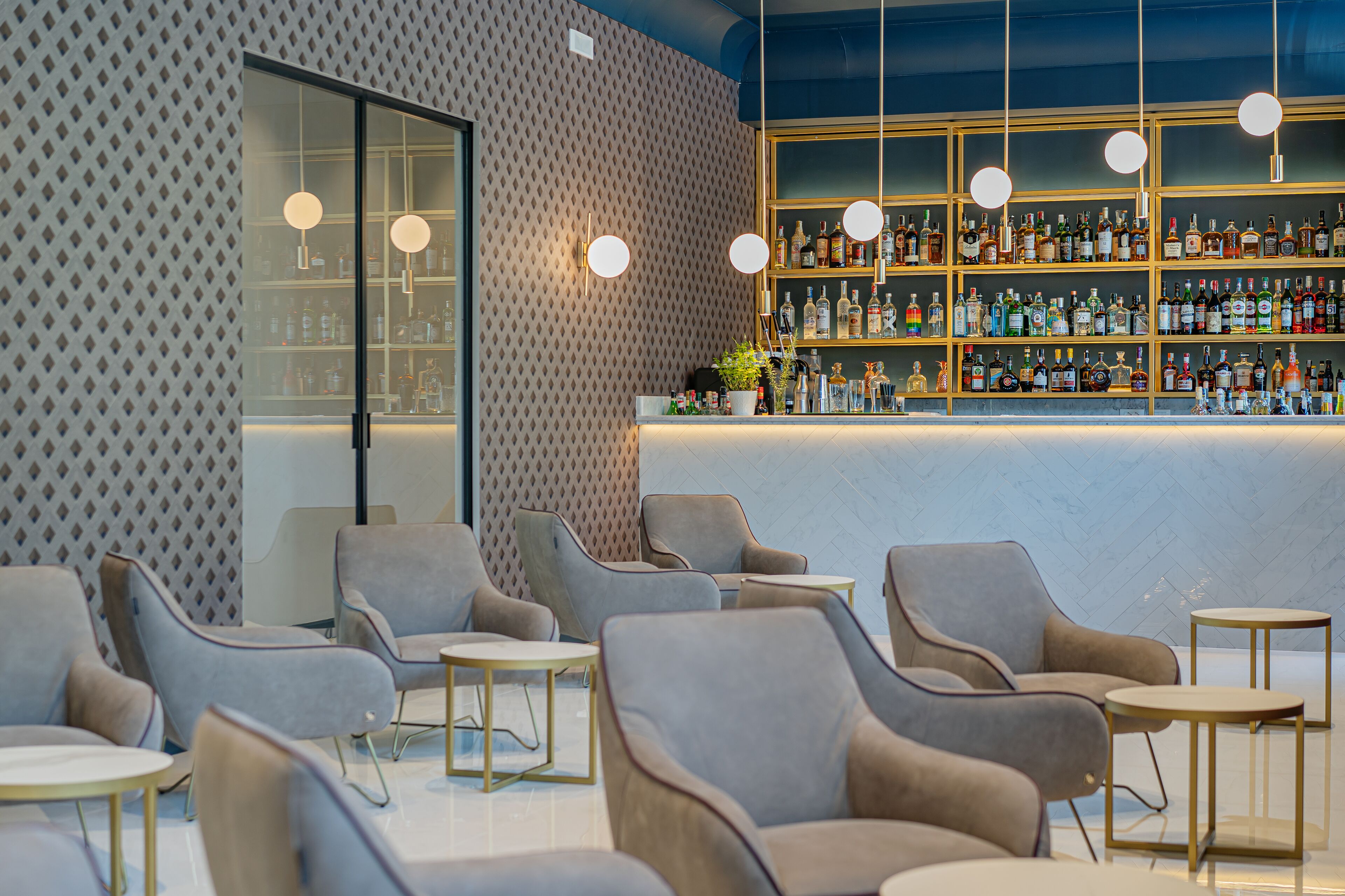 A modern bar area with a patterned wall, a variety of liquor bottles, and seating with round tables.