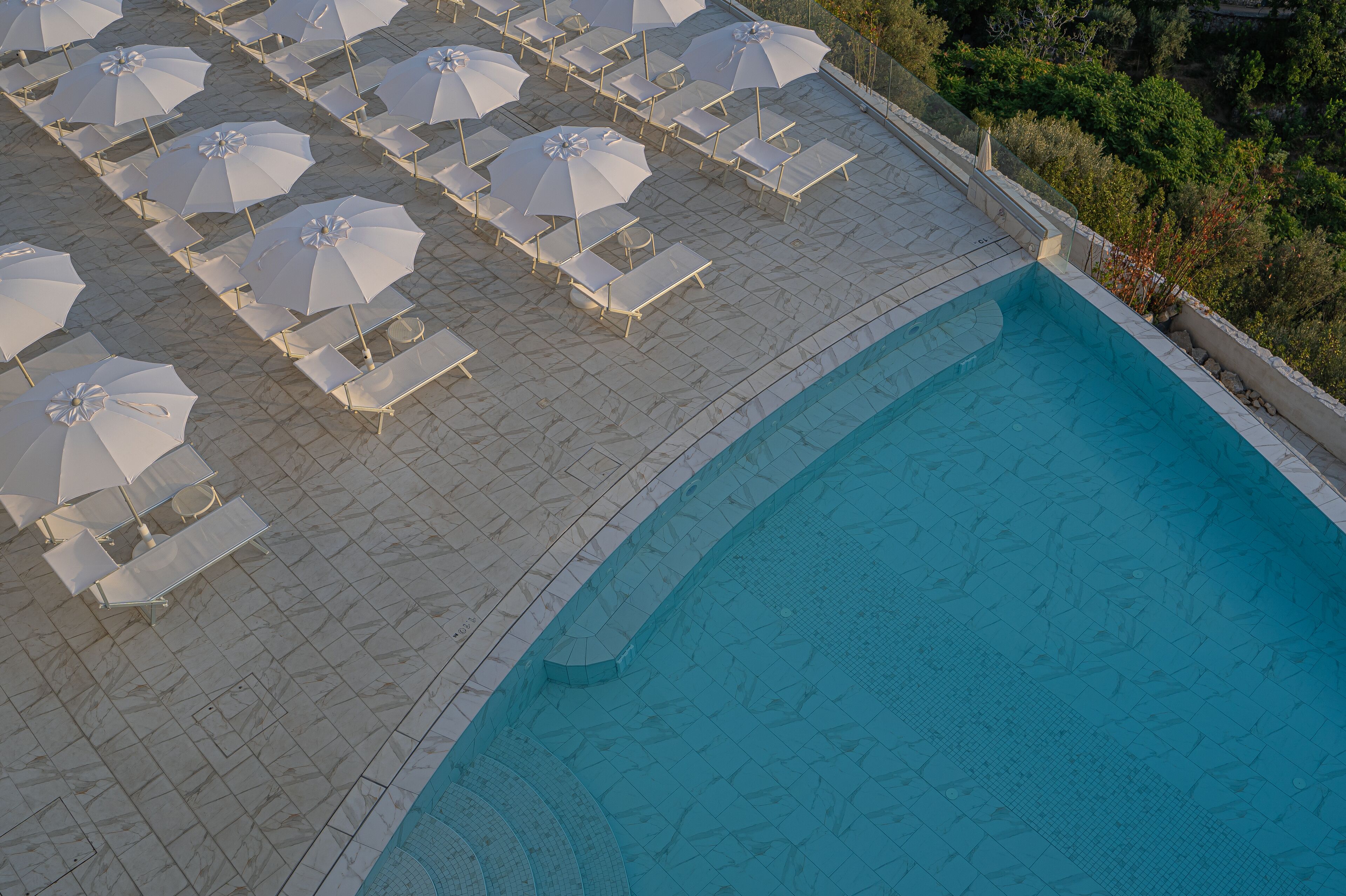 A swimming pool with white umbrellas and lounge chairs arranged around it.