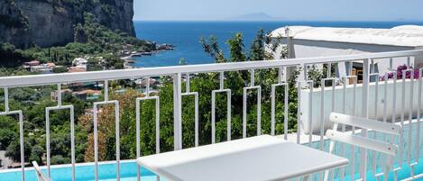 A poolside area with a table and chairs, overlooking a coastal landscape with a clear view of the sea and a cliff.