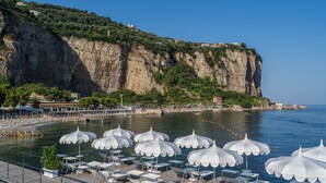 A seaside resort with white umbrellas and lounge chairs on a deck, overlooking a cliff and the sea.