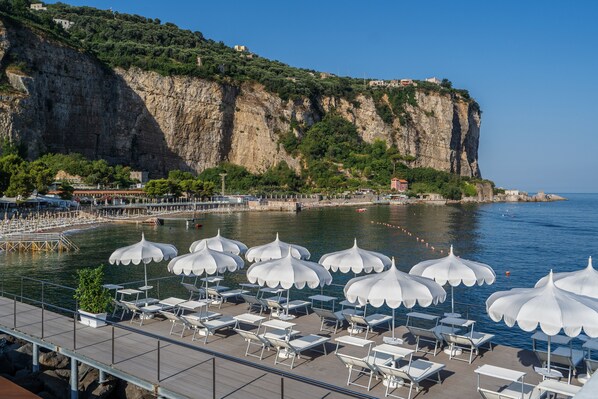 Une station balnéaire avec des parasols blancs et des chaises longues sur une terrasse, offrant une vue sur une falaise et la mer.
