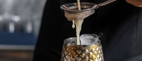 A person pouring a liquid from a metal container into a glass with a textured pattern.