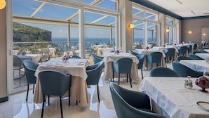 A restaurant with tables and chairs, large windows, and a view of the ocean.