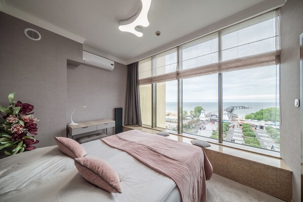 A modern hotel room with a large bed, a bedside table, a lamp, and a view of the sea and promenade. - Hotel Aurora Family & SPA (Miedzyzdroje)
