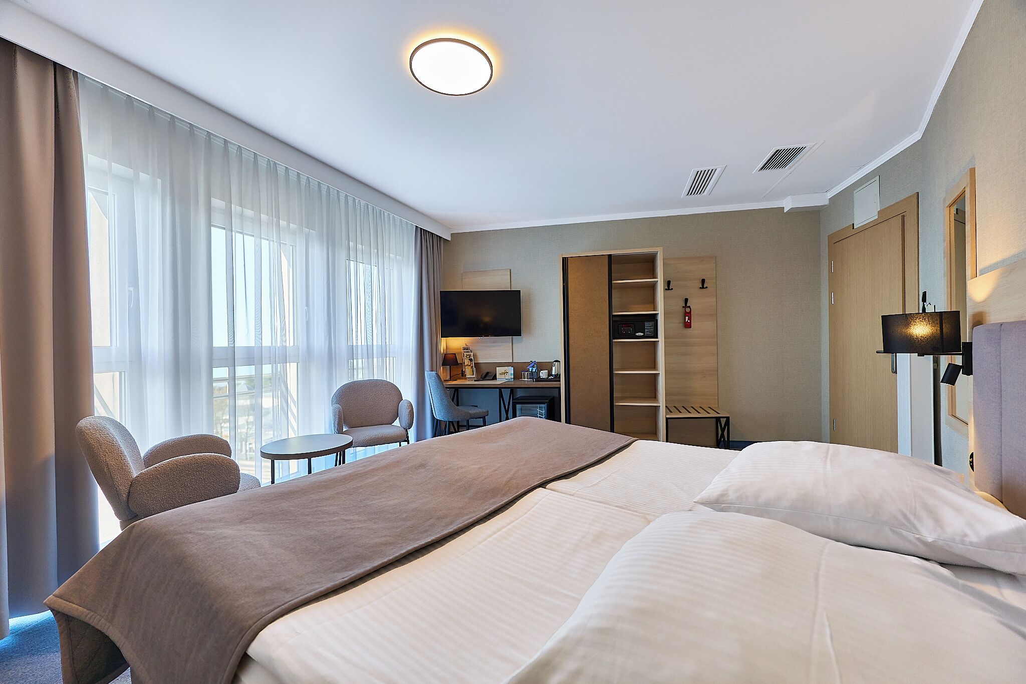 A hotel room with a bed, a desk, a chair, a TV, and a wardrobe.