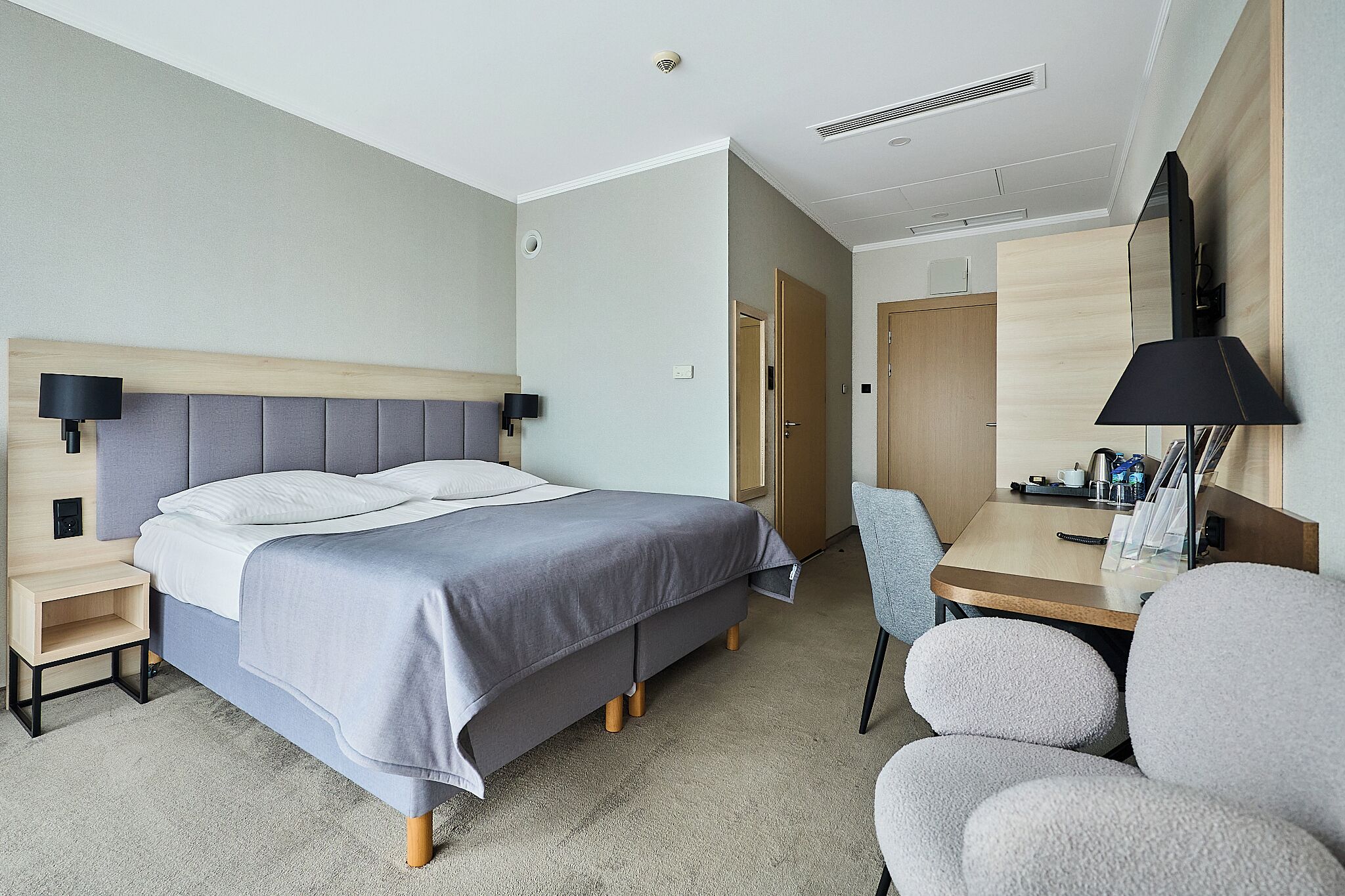 A hotel room with a bed, bedside table, chair, desk, and a mirror.
