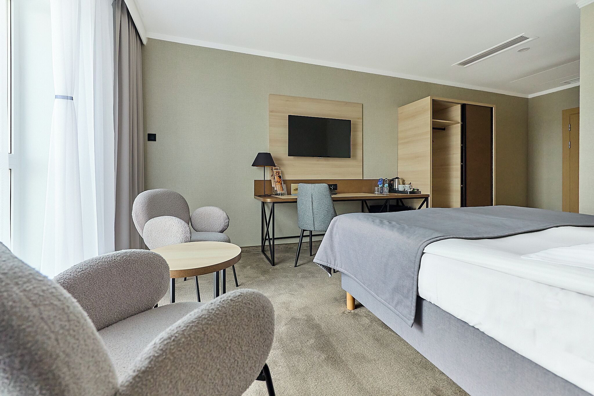 A hotel room with a bed, a desk, a chair, a TV, and a wardrobe.