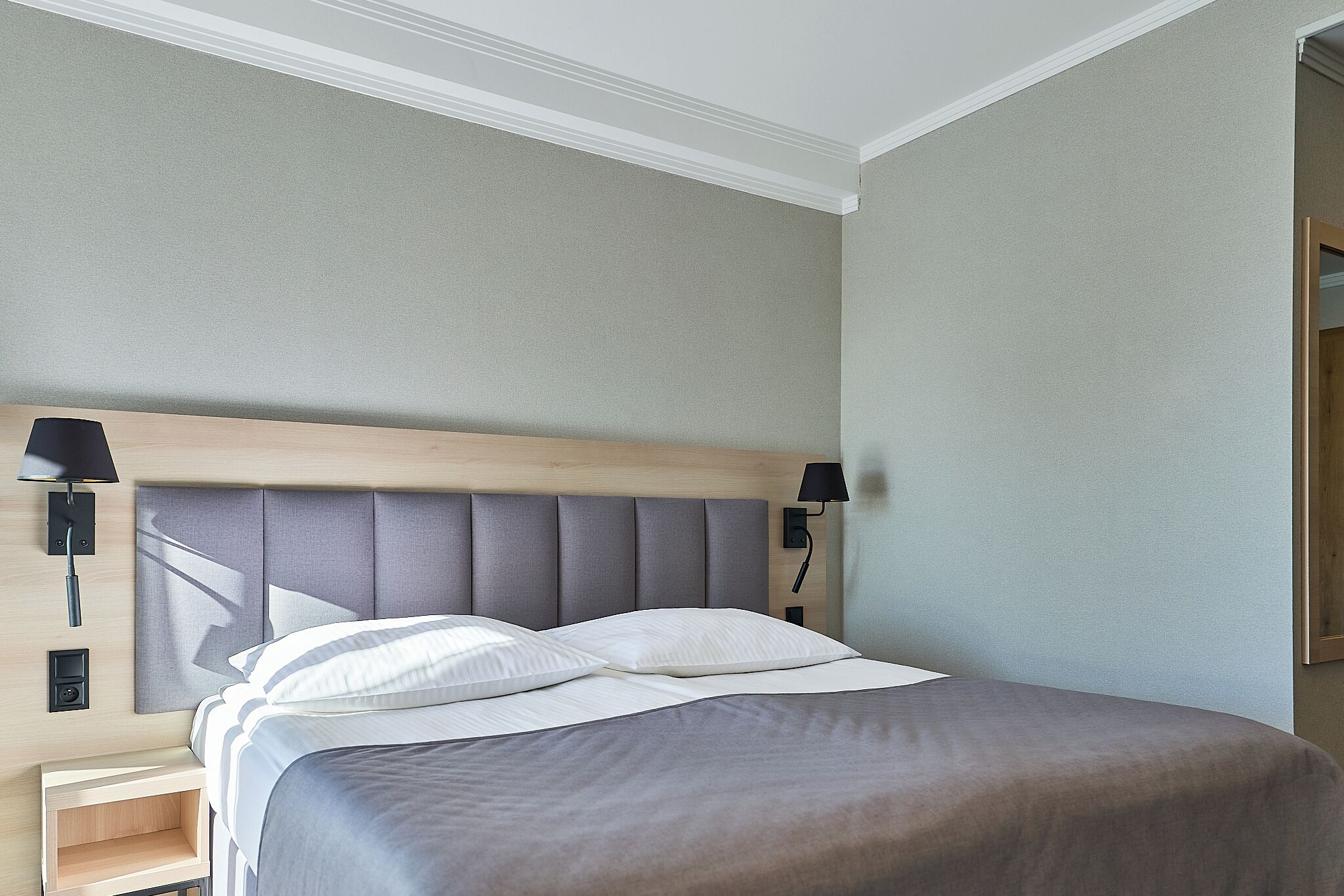 A neatly made bed with a headboard, two bedside lamps, and a small bedside table.