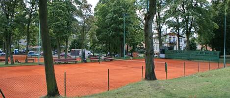 Una pista de tennis amb una tanca, bancs i arbres al fons.