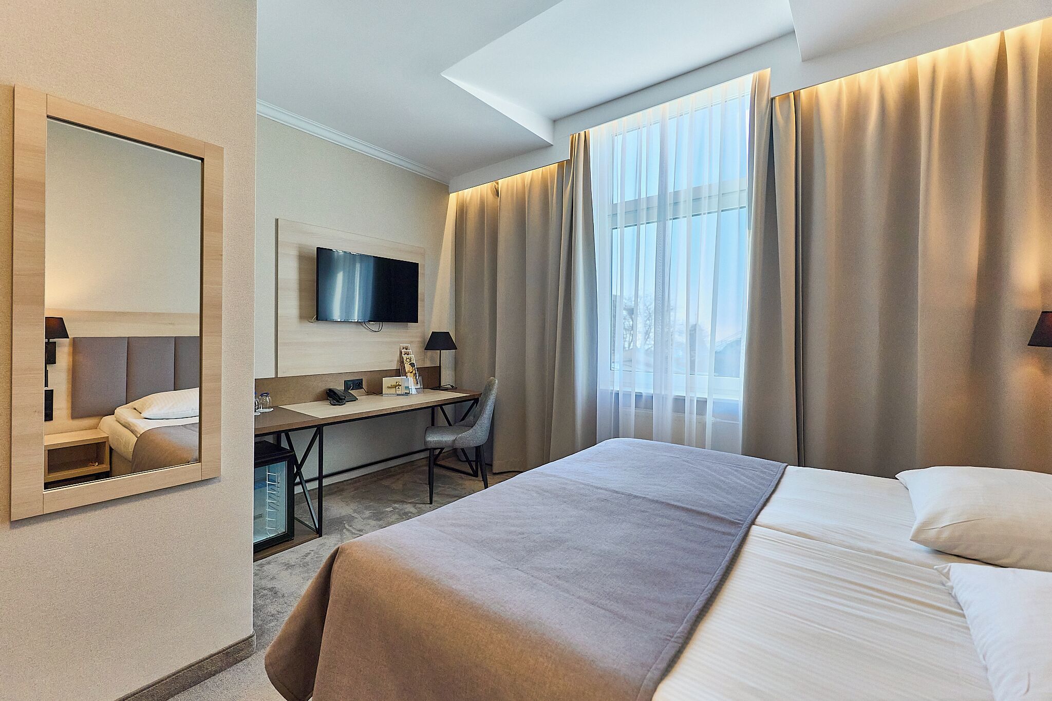 A hotel room with a bed, desk, chair, TV, and curtains.