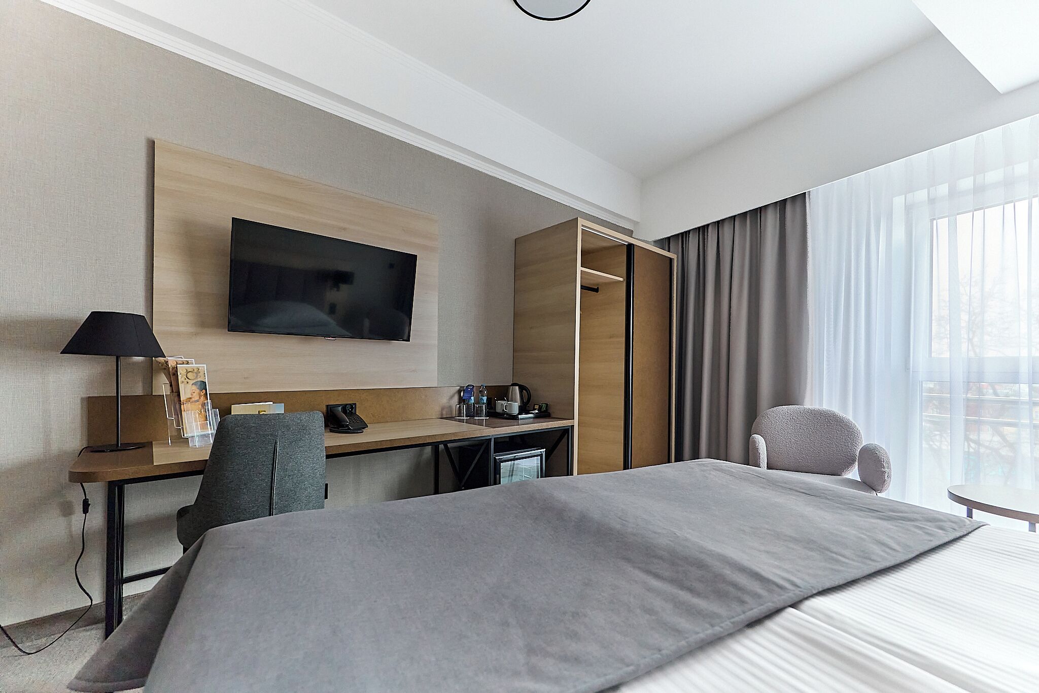 A hotel room with a bed, a desk with a computer, a TV, and a chair.
